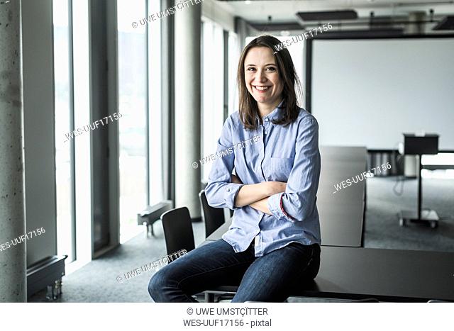 Portrait of smiling businesswoman sitting on conference table in office