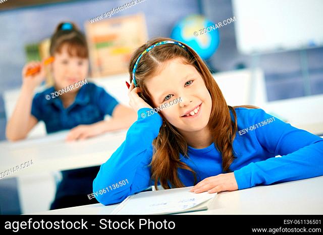 Laughing shcoolgirl sitting in class leaning on hand, other student in background