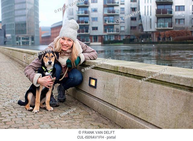 Portrait of mid adult woman and her dog on city riverside