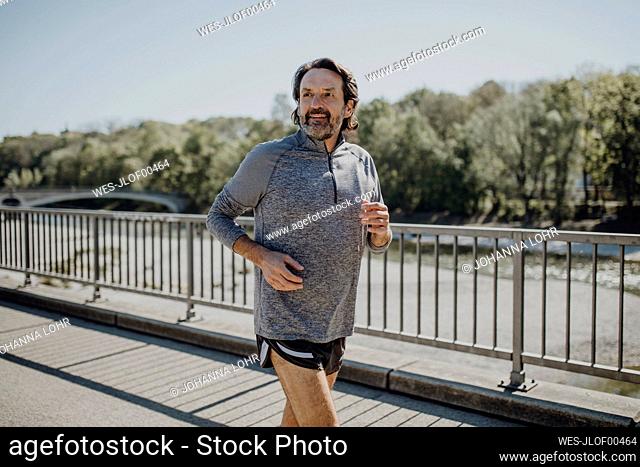 Smiling mature man running on road against clear sky in park during sunny day