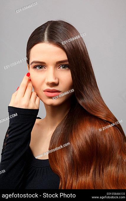 Closeup portrait of beautiful woman with luxurious and gorgeous brown hair posing over grey backhroung. Woman with modern hairstyle in studio