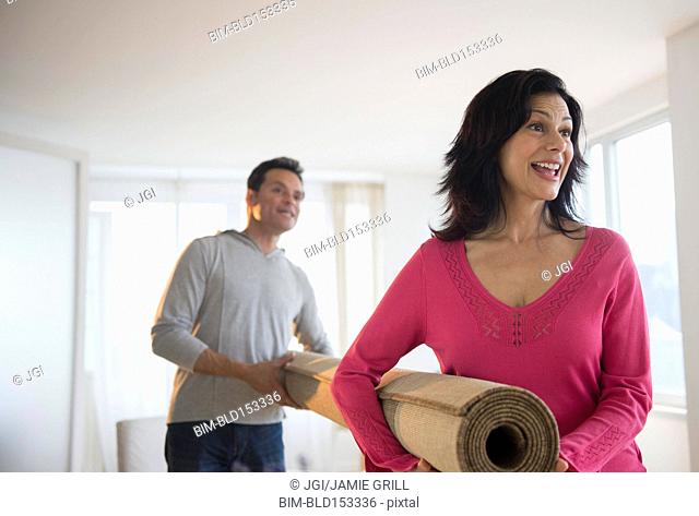 Couple carrying roll of carpet in living room