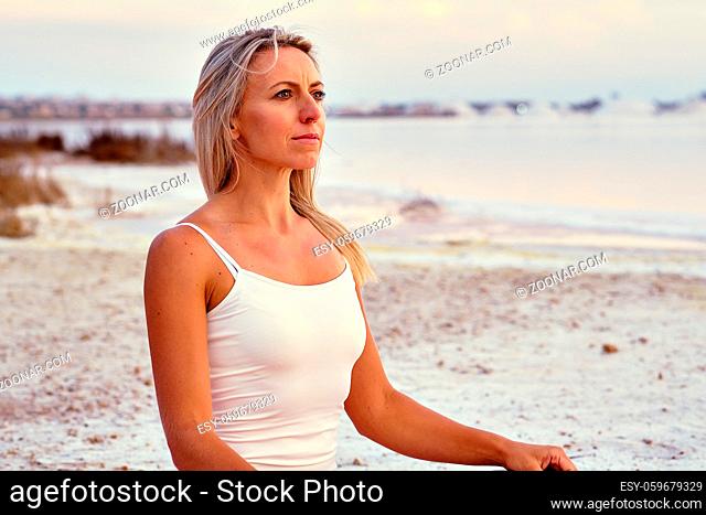 Calm alone middle-aged 50s yogi female wearing activewear seated in lotus pose meditates feel placidity doing yoga exercise on nature near lake