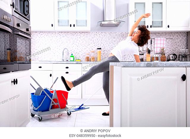 Close-up Of A Young African Woman Slipping While Mopping Floor In The Kitchen