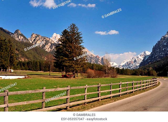 Landscape of Dolomites mountains in summer with a farm and meadows near a fence