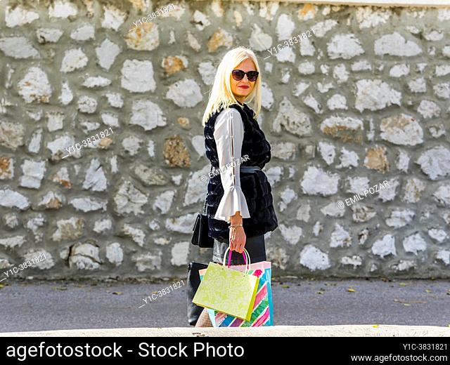 Attractive shopper blonde woman is walking along looking at camera, hands full