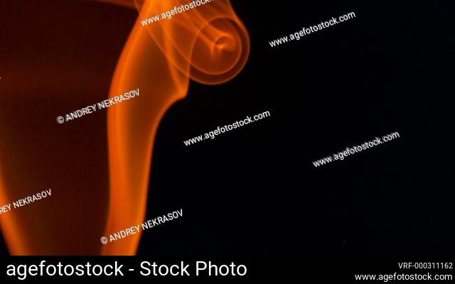 Thin trickle of fiery orange-red smoke slowly rising graceful twists up on black background. Colored smoke blowing from bottom to top. Closeup