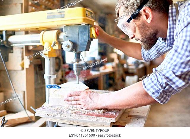 Side view portrait of mature bearded carpenter using drilling machine for piece of wood in modern workshop, copy space