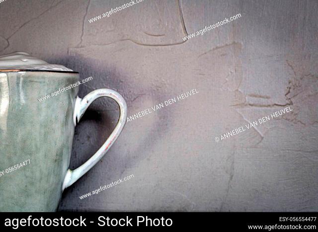 Ceramic mug with white foam gray natural stone design with concrete wall background, coffee or tea concept, copy space close up