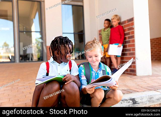 Multiracial elementary schoolboys studying while sitting on floor at school entrance