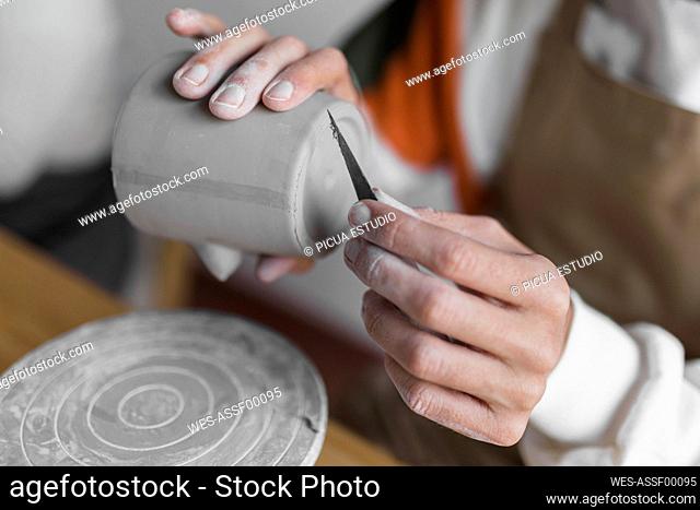 Male artist with clay cup and hand tool working at workshop
