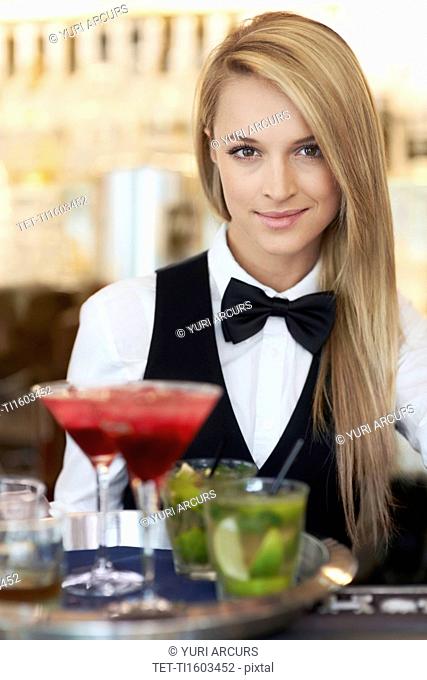 Portrait of female bartender holding tray with cocktails