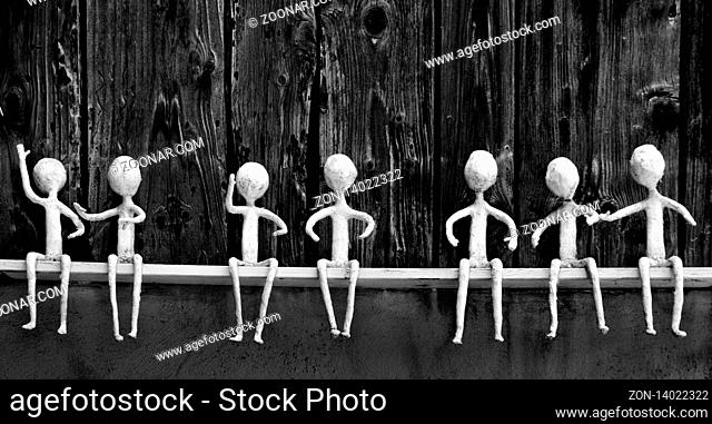 black and white view of seven white figures sitting on a wooden shelf in various poses