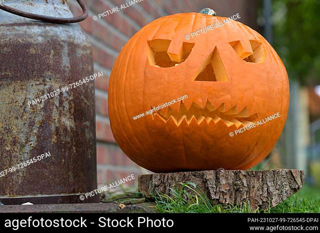 27 October 2023, Brandenburg, Potsdam: A carved pumpkin stands on the wall of a house. The light in the hollowed pumpkin is supposed to keep away the devil and...