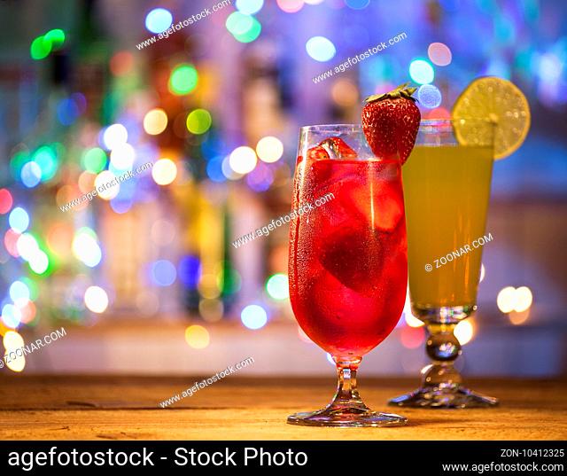 Glasses of strawberry and orange cocktails on a bar lights background