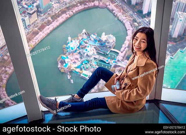 Asian lady travel and relax on the roof top bar out side windows is cherry blossom park in Seoul city with Sakura flower and tower background, Seoul, Korea