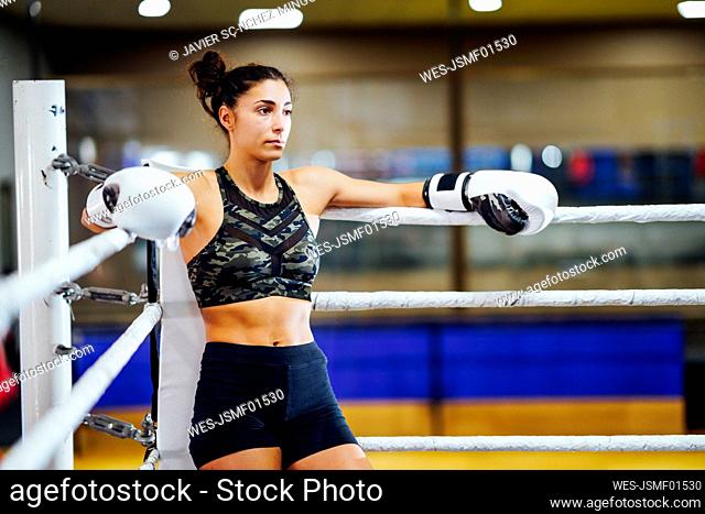 Athletic female boxer in boxing ring leaning on rope in the corner