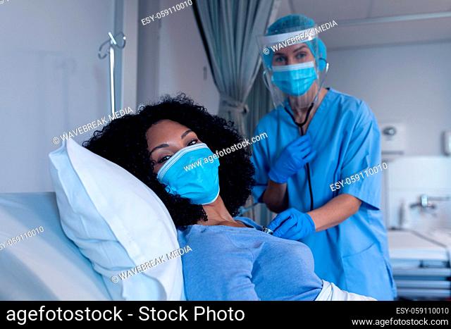 Caucasian female doctor in hospital in face mask examining female patient with stethoscope