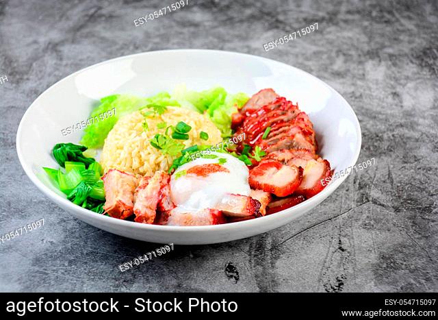 Barbecued red pork and crispy pork in red sauce, served with rice and vegetable on white plate.