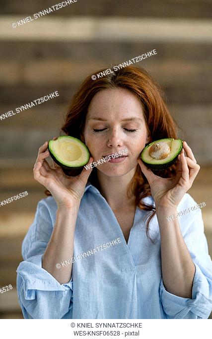 Portrait of redheaded woman with eyes closed holding sliced avocado
