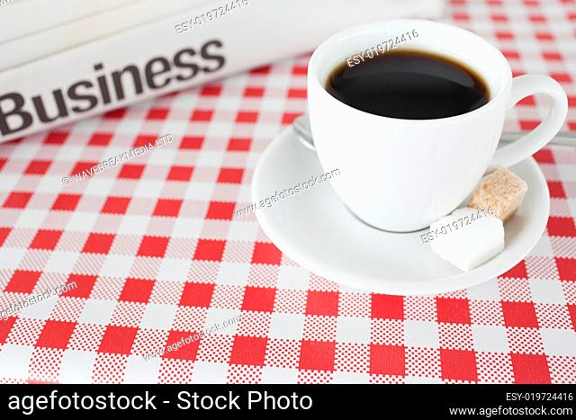 A cup of coffee and a newspaper on a tablecloth