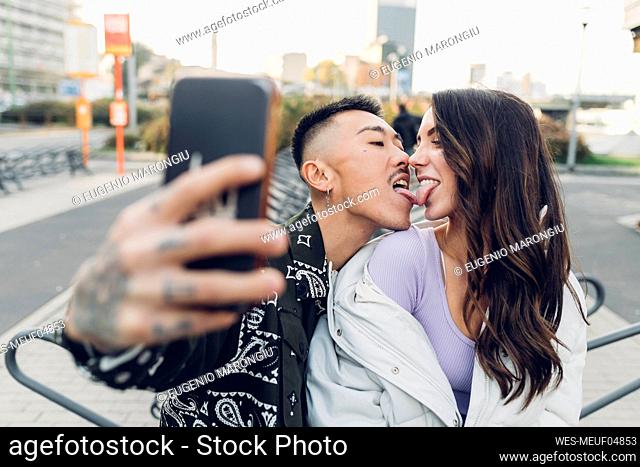 Affectionate couple touching tongues and taking selfie through smart phone