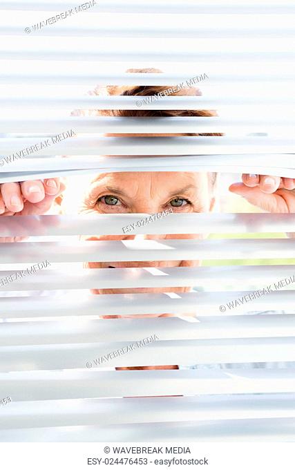 Portrait of mature woman looking through blinds