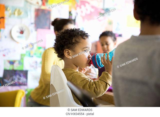 Cute, innocent baby boy drinking from sippy cup at table