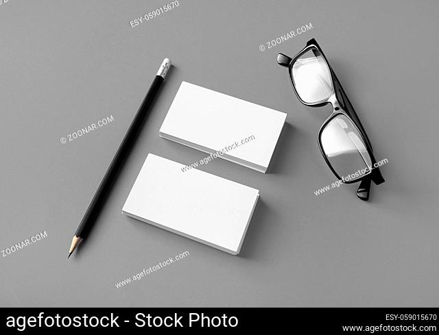 Blank business cards, pencil and glasses on gray paper background. Mockup for ID