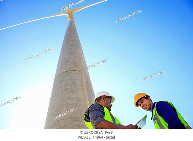 Low angle view of technicians with tablet in front of wind turbine