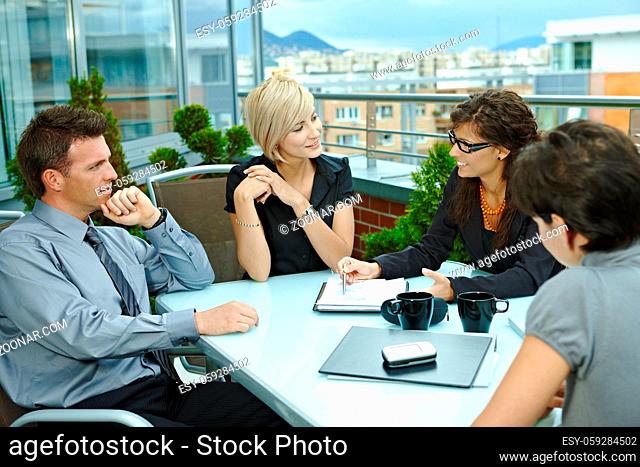 Group of young business people sitting around table on office terrace outdoor, talking and working together