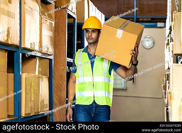Portrait of Indian asian warehouse worker hold cardboard box packaging on his shoulder in warehouse distribution center environment