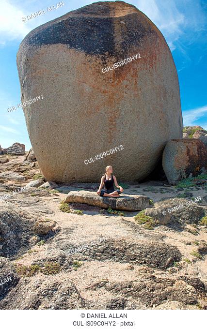 Young woman practicing lotus yoga pose on beach rock, Cape Town, Western Cape, South Africa