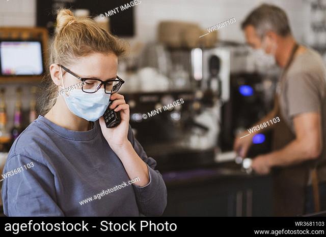 Blond waitress wearing face mask working in a cafe, on the phone