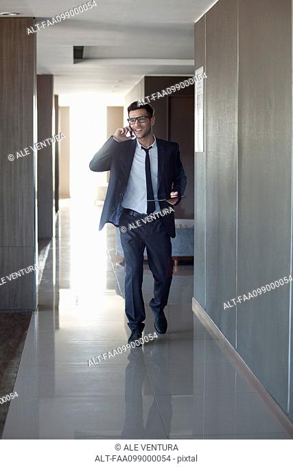 Young businessman talking on phone while walking through office