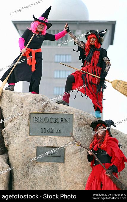 30 April 2022, Saxony-Anhalt, Schierke: Three women dressed as witches stand on the Brocken at the official height marker in front of the Brocken Hotel