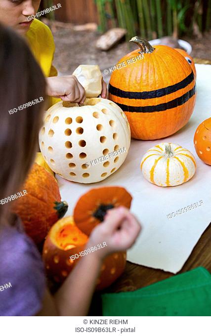 Over shoulder view of girl and brother preparing pumpkins on garden table