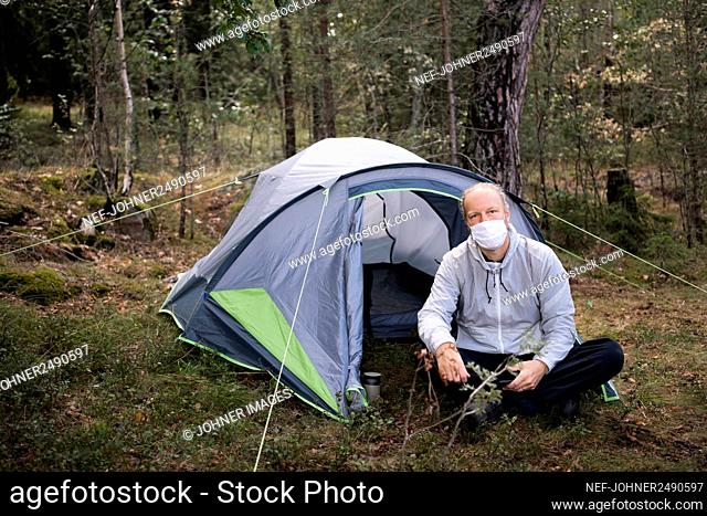 Man wearing face mask sitting in front of tent