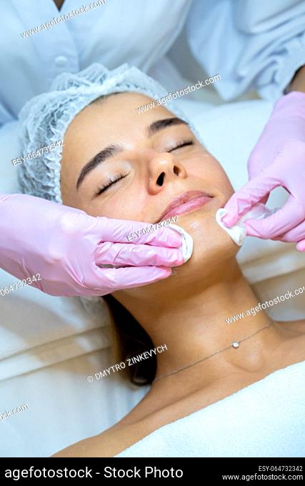 Unrecognizable beautician doctor cleaning woman face with cotton pads, skin care procedures, rejuvenation