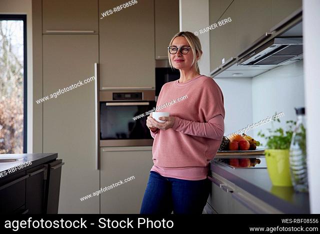 Blond woman holding coffee cup standing in kitchen
