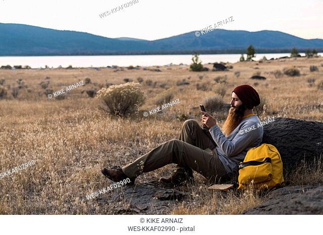 USA, North California, bearded young man using cell phone during a break on a hiking trip near Lassen Volcanic National Park