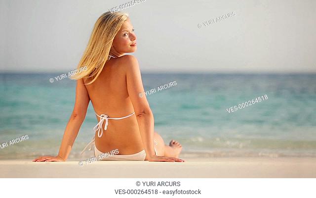 Footage of an attractive young woman relaxing on the beach looking at you over her shoulder