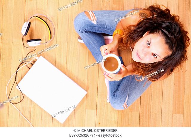 A girl sitting on the floor with a Laptop and some coffee