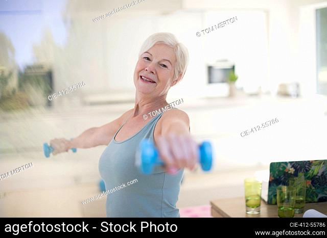 Portrait confident senior woman exercising with dumbbells in kitchen