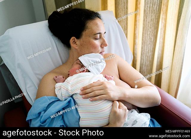 Mother embracing newborn baby boy while resting