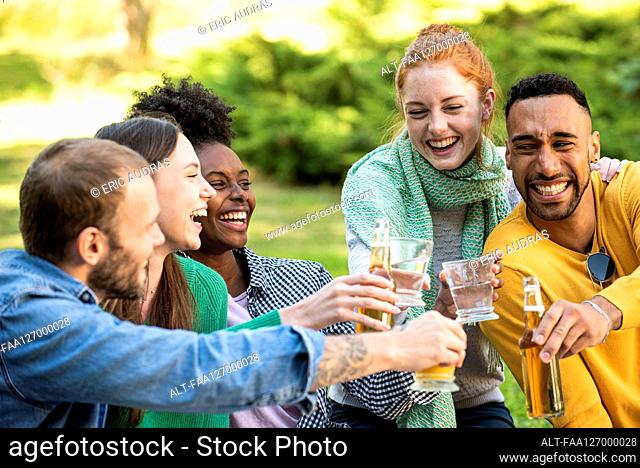 Happy young friends toasting drinks in garden