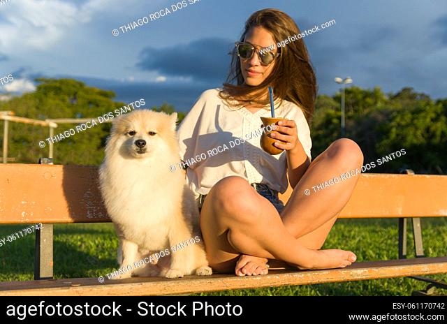 Blonde woman taking traditional gaucho chimarrao with dog in the park