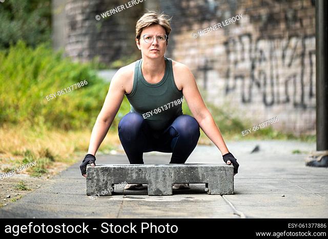Portrait of a sporty 36 year old white woman lifting a heavy construction block, Brussels, Belgium