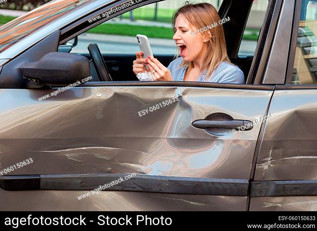 Profile of angry despaired female with blonde hair holding smart phone in hands and screaming loudly while calling to insurance service after road accident