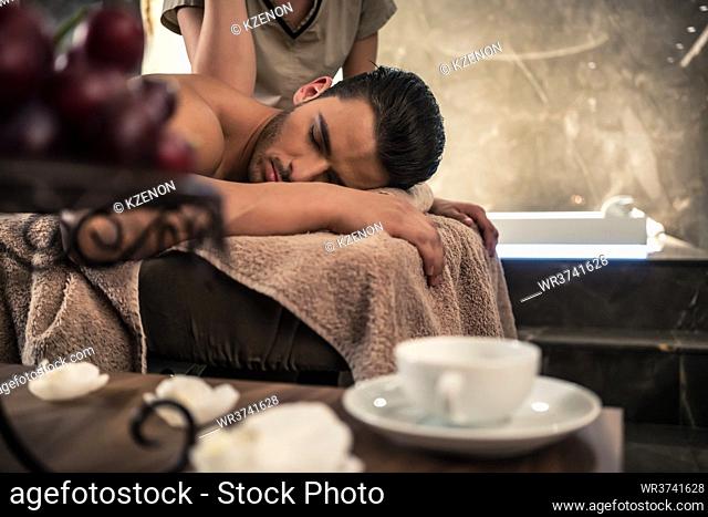 Young man lying down during traditional acupressure procedure of Thai massage at luxury spa and wellness center